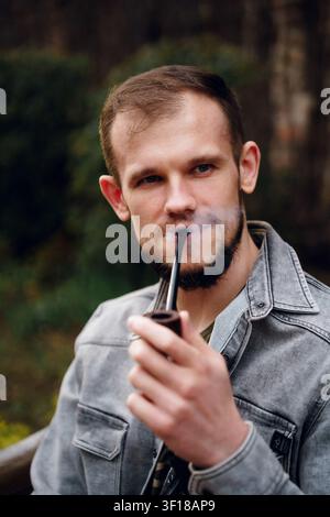 Portrait Of A Thoughtful Bearded Man Smoking A Wooden Pipe In A Forest Outdoor Setting Stock Photo