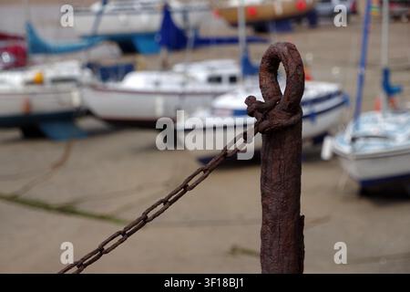 Very old rusty post and chain at Elie Beach with out of focus boats in the background Stock Photo