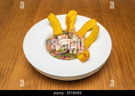 Traditional Peruvian Seafood Ceviche with Shrimp and Red Onion in Citrus Marinade Decorated with Golden Fried Plantain Slices on a White Plate Over Wo Stock Photo