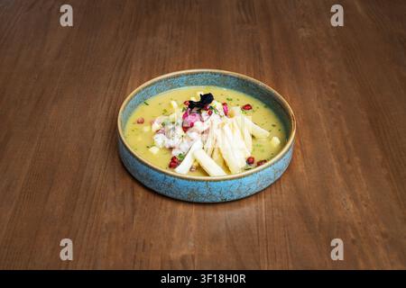 Contemporary Ceviche Dish Featuring Diced White Fish, Pomegranate Seeds, and Golden Yucca Sticks in a Rich Yellow Marinade Presented in a Textured Blu Stock Photo