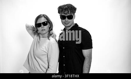 Young man and woman posing together in black and white studio portrait wearing sunglasses Stock Photo