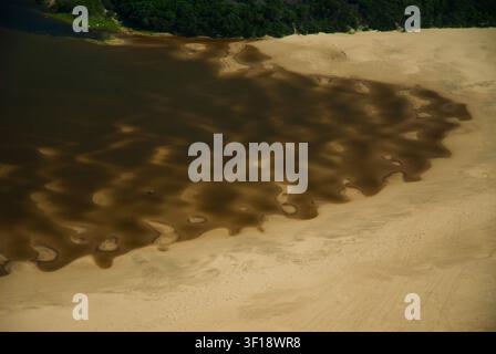 An aerial view of a river mouth flowing into a sandy coastal area along the Eastern Cape coast of South Africa. Dark river water spreads across pale s Stock Photo