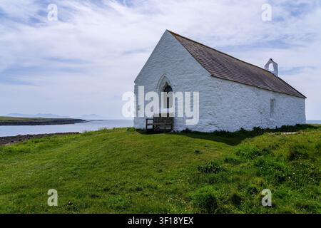 The Medieval church of Eglwys Cwyfan stands on Cribinau island in Anglesey surrounded by blooming pink thrift wildflowers. Stock Photo