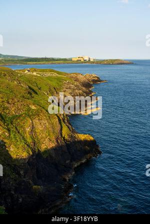 The rocky cliffs of Cemaes Bay overlook the Irish Sea with the distant Wylfa Nuclear Power Station on the Anglesey coast of North Wales. Stock Photo