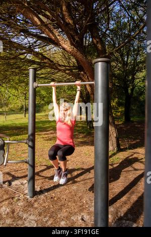 Woman performing an exercise hanging from a pull-up bar in an outdoor forest gym Stock Photo