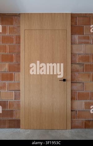 Plain wooden door set in textured red brick wall with dark handle and minimalist design Stock Photo