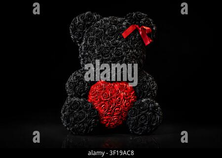 Black rose teddy bear holding a red rose heart on black background Stock Photo