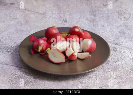 Fresh red radishes, whole and sliced, on a dark plate, representing healthy food ingredients and organic produce Stock Photo