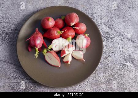 Fresh red radishes, whole and halved, on a dark grey plate, ready for healthy eating Stock Photo