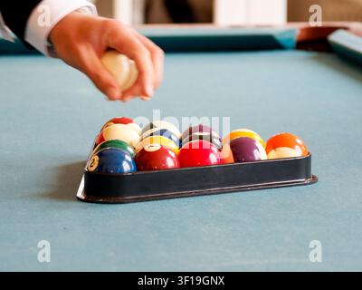 Billiard balls arranged in a triangle rack on a pool table with player holding cue ball Stock Photo