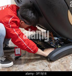 Technical expert measuring and repairing electronic motherboard of luxury massage chair with professional multimeter and soldering iron tools. Stock Photo