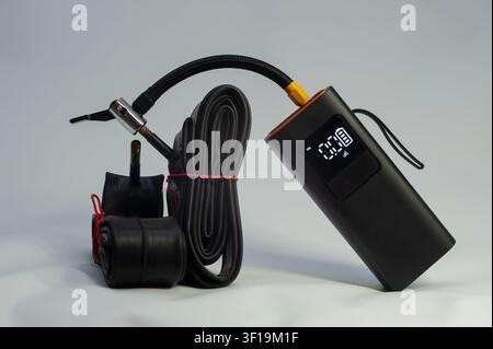 Portable electric tire inflator with digital pressure display, flexible air hose and bicycle tube on dark background, modern air pump for inflating bi Stock Photo