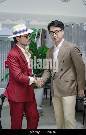 Two handsome Asian business partners in classic tailored suits shaking hands and talking outdoors, elegant gentlemen lifestyle and friendship concept Stock Photo