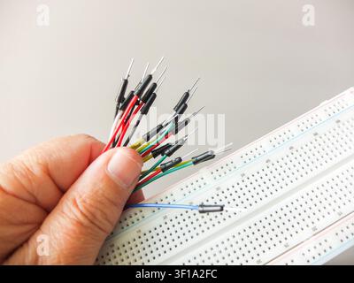 Hand holding a bunch of colorful jumper wires next to an electronic breadboard. Stock Photo