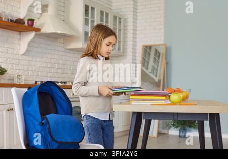 Child preparing colorful school books beside a blue backpack on wooden table Stock Photo