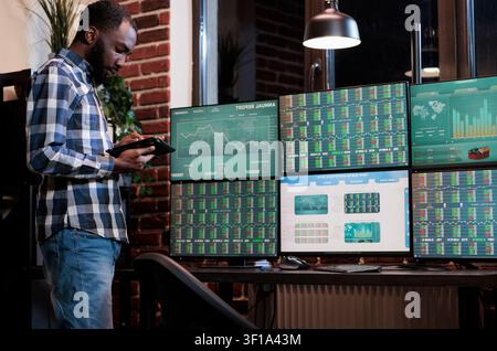 Investor analyzing stock options on tablet, african american hedge fund trader in agency workspace having touchscreen device, showing financial data, focused on investor analyzing. Stock Photo