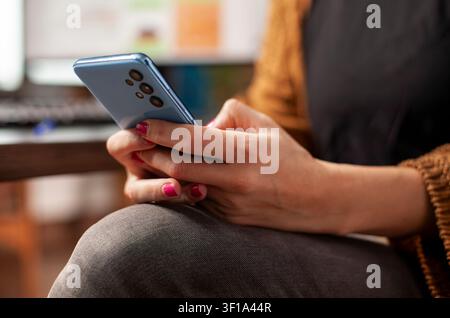 Female office worker types on a smartphone during working hours, with selective focus on hands, mobile messaging and social media use at a startup desk. Stock Photo