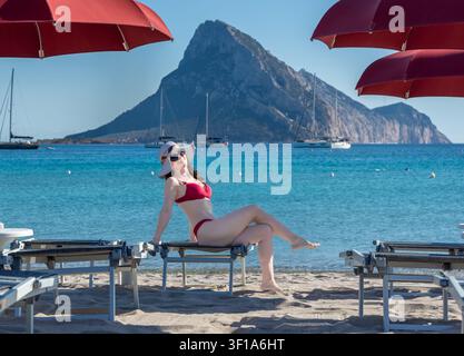 Young woman relaxing on a sun lounger at La Cinta Beach with Isola Tavolara, San Teodoro, Sardinia, Italy Stock Photo