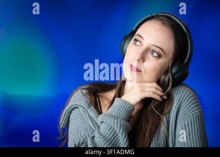 Young Woman Lost in Thought Listening to Music with Wireless Headphones Stock Photo