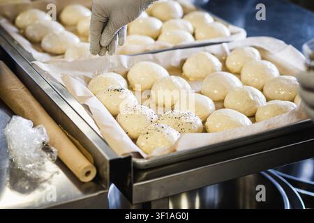 Baker Sprinkling Seasoning on Fresh Sourdough Bread Rolls Before Baking Stock Photo
