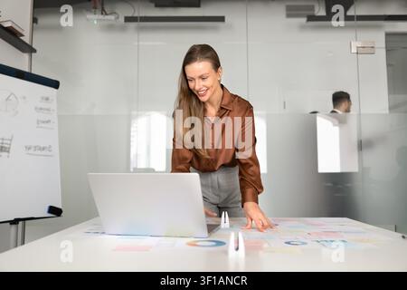 Businesswoman stands at desk working on strategy using laptop Stock Photo