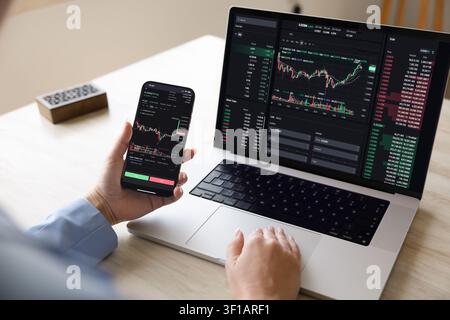 Trader using laptop and smartphone displaying financial trading charts Stock Photo