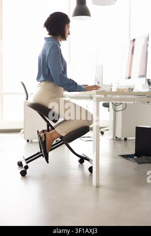 Employee working at computer in office seated on ergonomic chair Stock Photo