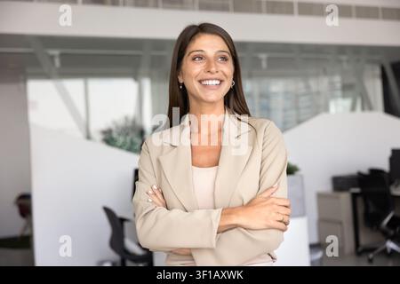 Happy Latina businesswoman standing in workspace with folded arms Stock Photo