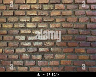 A wall made of bricks shows various shades of red and brown with a textured surface. The setting represents classic construction. Stock Photo