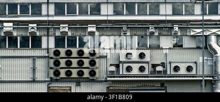 Industrial building facade presenting a detailed view of air conditioning units, ventilation ducts, and various piping Stock Photo