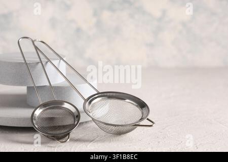 Two stainless steel tea strainers with fine mesh on a light textured background, kitchen utensils for sifting and brewing Stock Photo