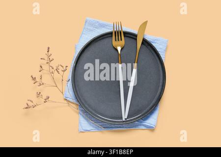Modern black ceramic plate with gold and white cutlery, light blue napkin, and dried floral branch on a peach background Stock Photo