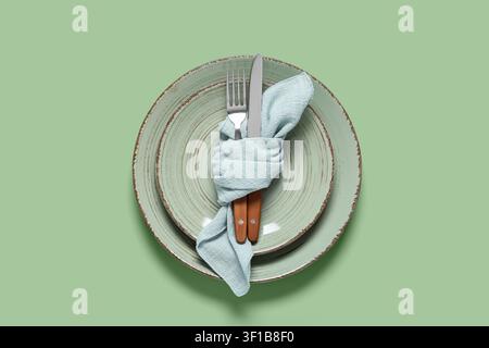 Elegant table setting with two rustic green plates, light blue napkin, and wooden handle cutlery on a solid green background Stock Photo