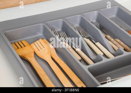 Kitchen drawer with organized cutlery and wooden utensils in a gray plastic organizer tray, the drawer contains metal forks and knives with light wood Stock Photo