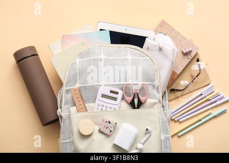 Stylish school backpack with different stationery supplies, thermos and modern tablet computer on beige background Stock Photo
