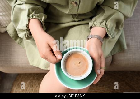 Woman in a green dress holding a cup of coffee with a mint green saucer, comfort and relaxation concept, the hot beverage provides a moment of leisure Stock Photo