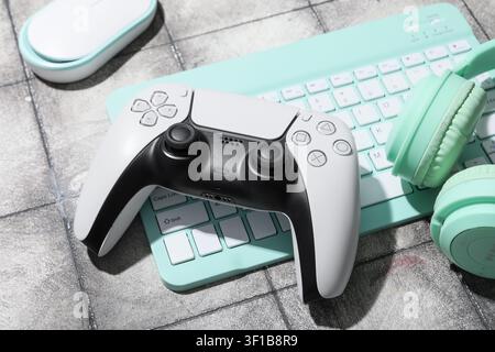White and black video game controller with mint green keyboard, headphones, and mouse on a gray background Stock Photo