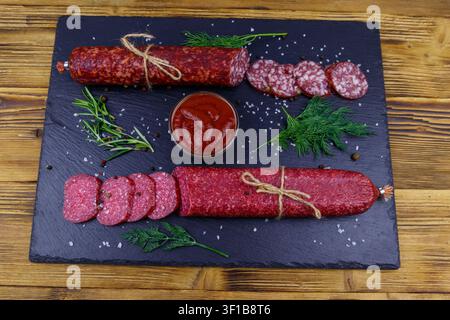 Salami sausages with ketchup and spices on black slate board on a wooden table Stock Photo
