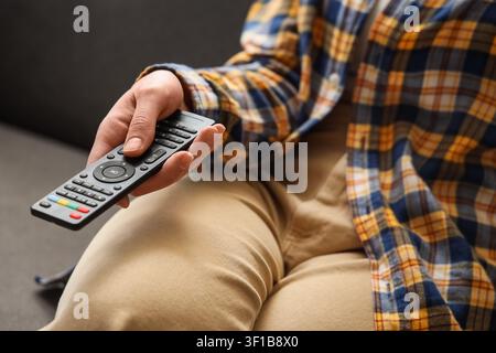 Person in plaid shirt holding a modern black remote control, home entertainment and relaxation concept, Act of changing channels or adjusting settings Stock Photo