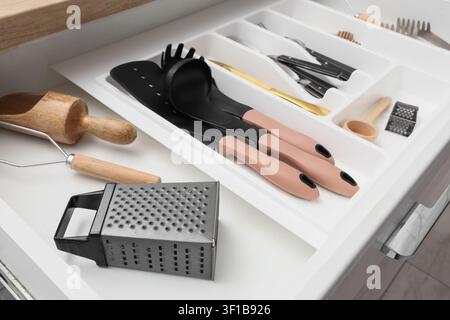 Kitchen drawer with organized cooking utensils and cutlery in a white plastic organizer tray, the drawer contains black silicone spatulas and a ladle Stock Photo