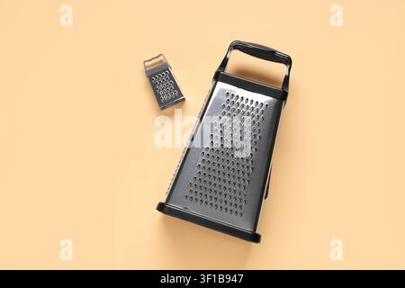 Two stainless steel box graters, one large and one small, with black handles on a light orange background Stock Photo