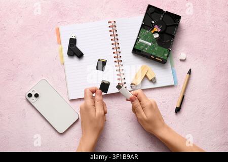 Hands holding a usb flash drive and sd card with various data storage devices on a pink background, this composition illustrates modern technology, el Stock Photo
