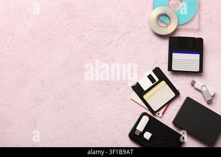 Evolution of data storage devices with floppy disks, usb flash drives, and cds on a pink background Stock Photo