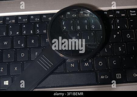Magnifying glass hovering over a modern computer keyboard close-up Stock Photo