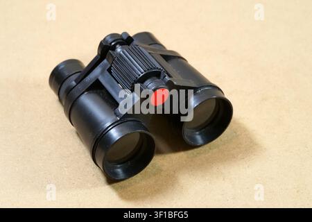 Small black plastic toy binoculars with red center detail on a brown surface, close-up of a children’s observation, exploration and pretend play acces Stock Photo