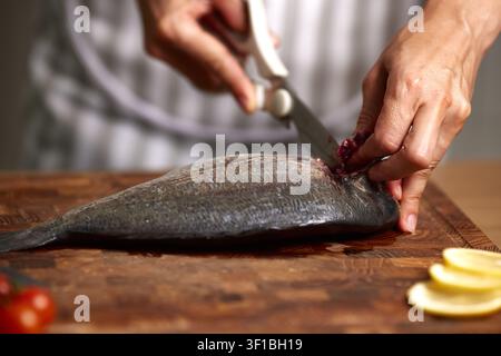 Hands cutting fresh raw sea bream on wooden board Stock Photo