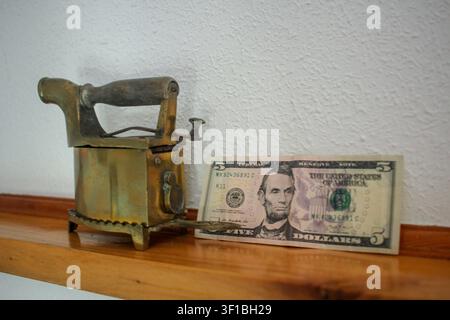 An evocative still life featuring a US five dollar bill placed beside an old fashioned brass iron on a wooden mantelpiece, illustrating themes of hist Stock Photo