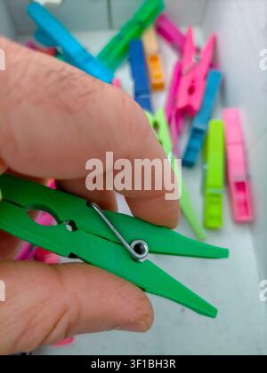 A detailed shot capturing a hand choosing a green peg from a collection of vibrant plastic clothespins, perfect for themes related to domestic work, c Stock Photo