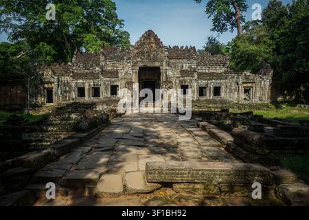 A wide, straight path of large, uneven gray stone blocks leads towards a weathered sandstone temple with multiple dark rectangular openings and intric Stock Photo