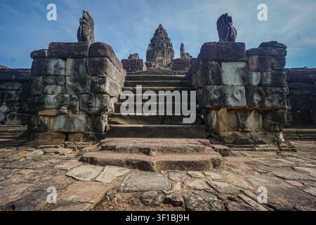A wide, weathered gray stone staircase ascends between two large, rectangular stone blocks, each topped with a dark, carved stone animal statue. The b Stock Photo